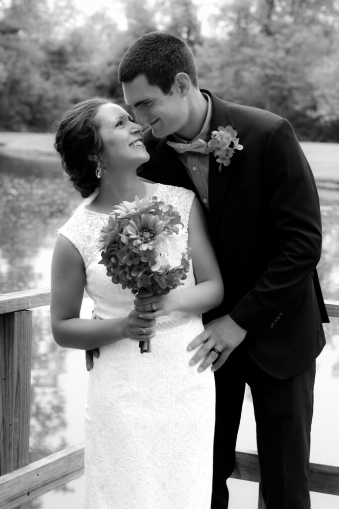 young couple holding each other on wedding day by pond smiling at each other