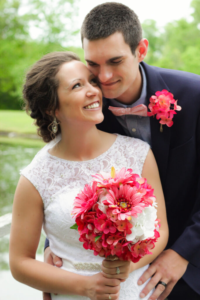 young couple holding each other on wedding day by pond smiling at each other