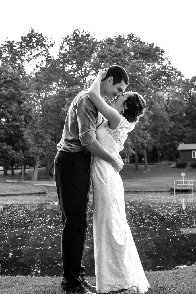 young couple on wedding day kissing by pond