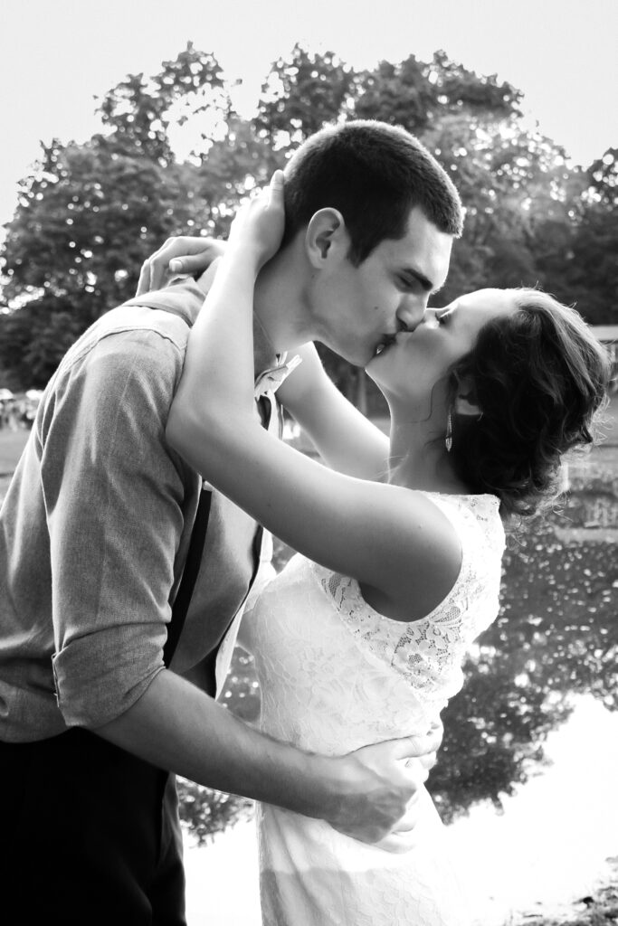 young couple on wedding day kissing by pond