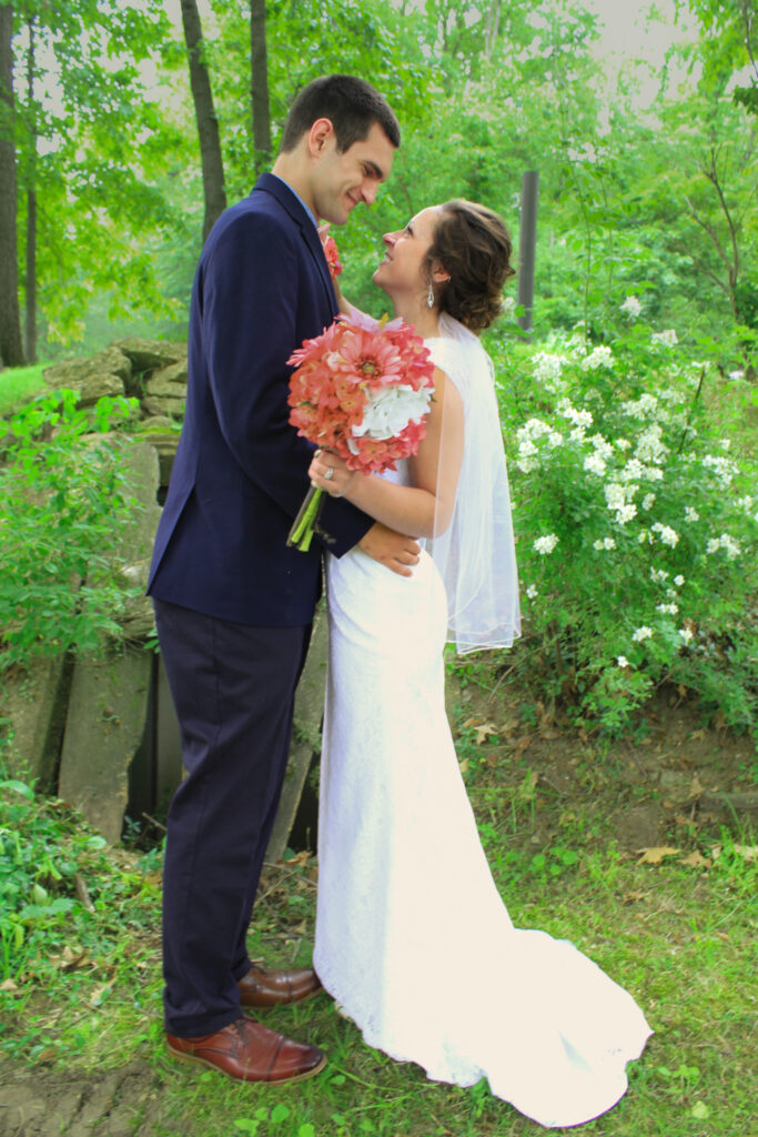 young couple on wedding day smiling at each other in woods