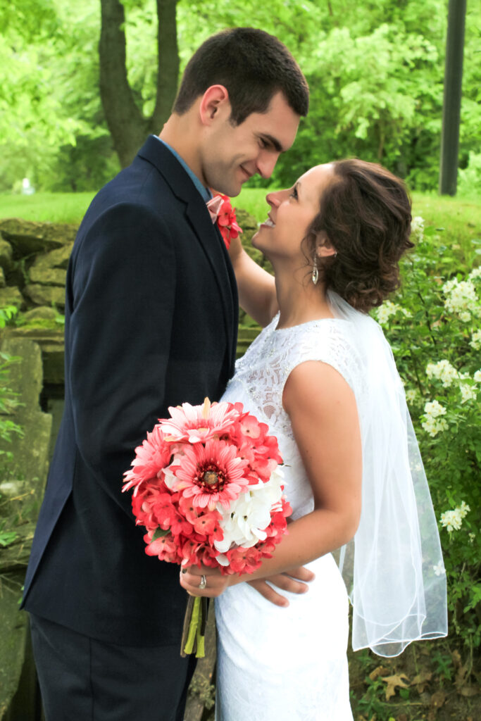 young couple on wedding day smiling at each other in woods