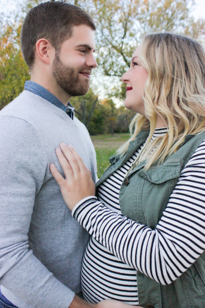 Couple looking at each other with love, husband's hand is on wife's pregnant belly and wife's hand is on husband's chest