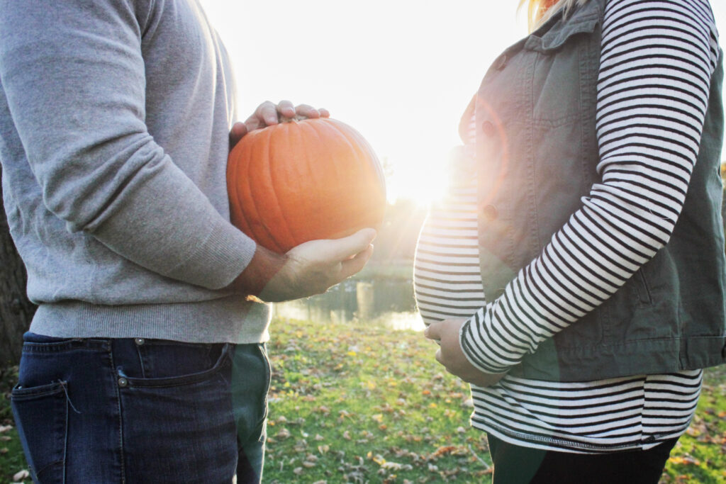 Couple facing each other, wife is holding belly and husband is holding pumpkin