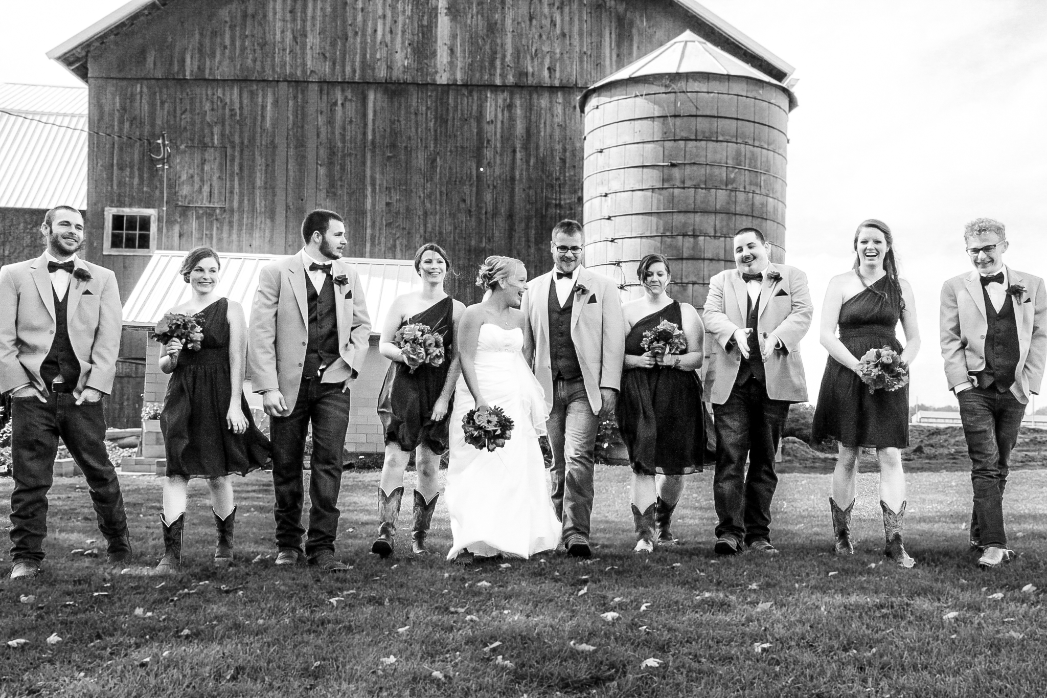 Bride and groom walk towards camera with bridal party, rustic barn as background