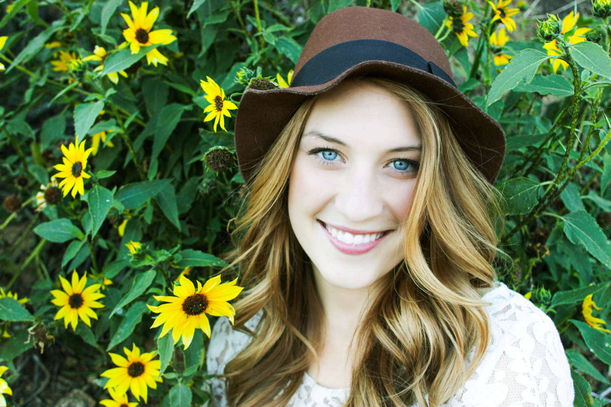 College senior photo of girl with hat smiling in front of flowers