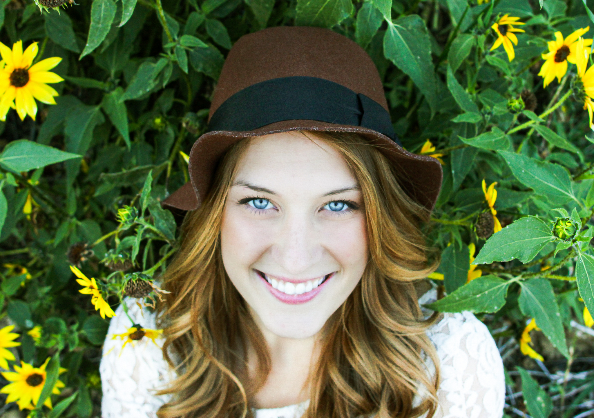 College senior photo of girl with hat smiling in front of flowers