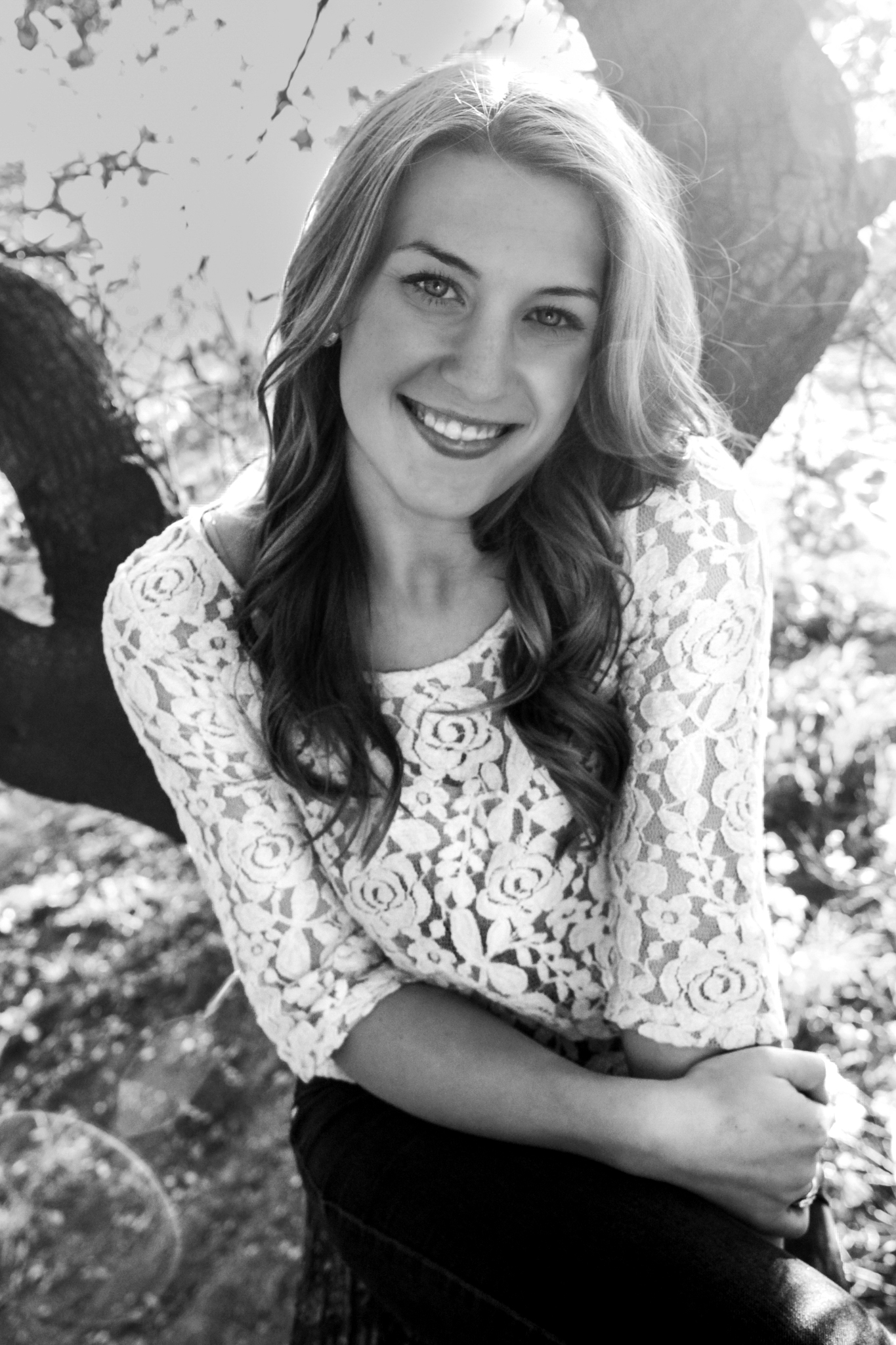 College senior photo of girl sitting in front of a tree smiling