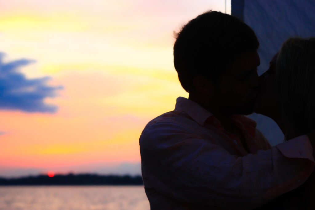 Young silhouetted couple kiss on a sailboat during sunset