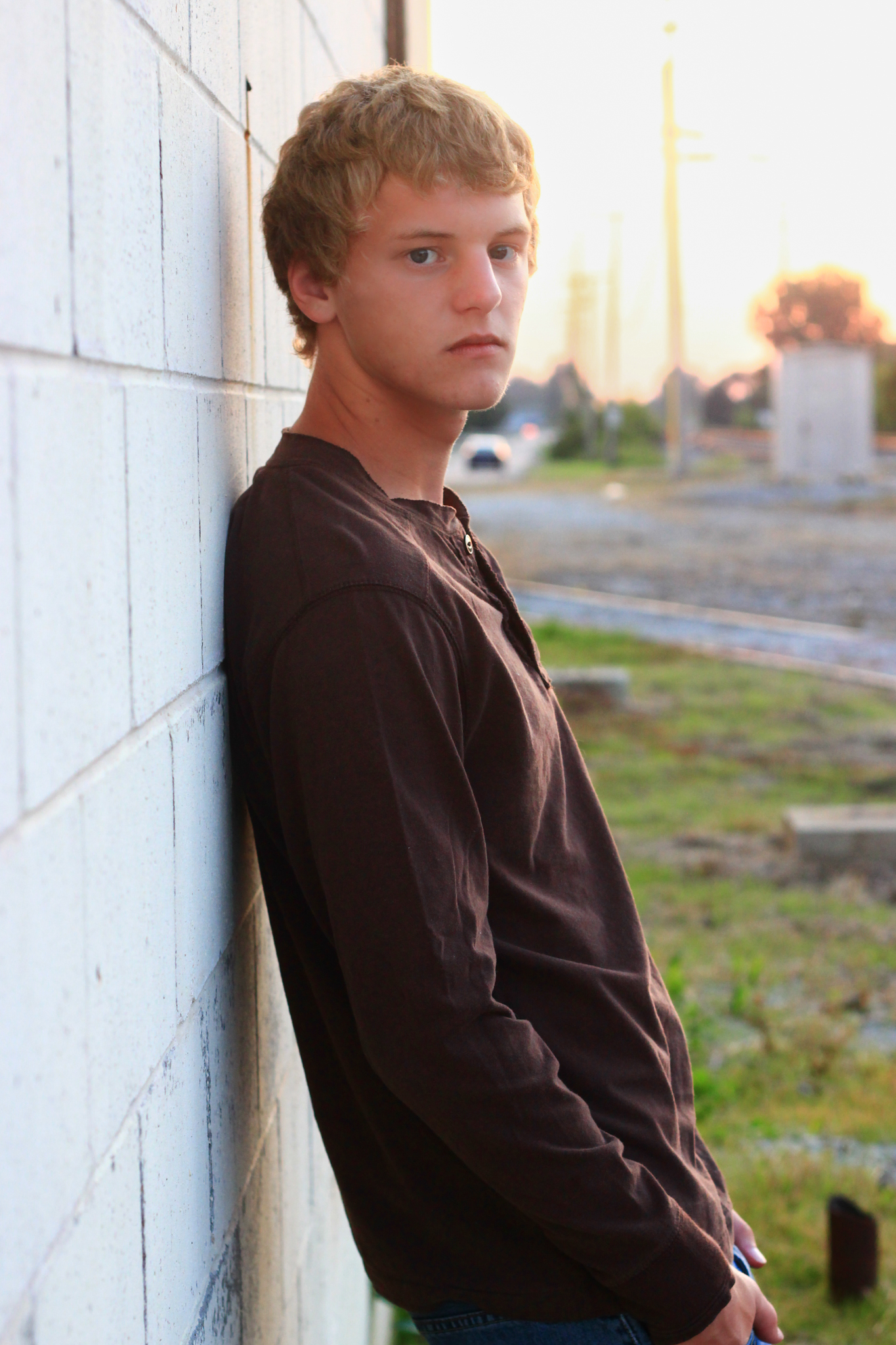 Young man leans against white brick wall for a senior photo