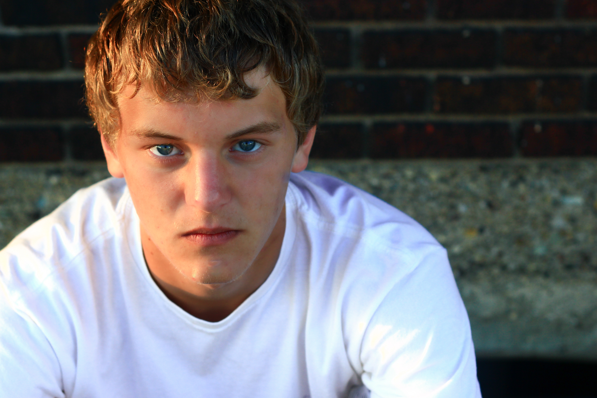 Young man sits against brick wall for senior photo