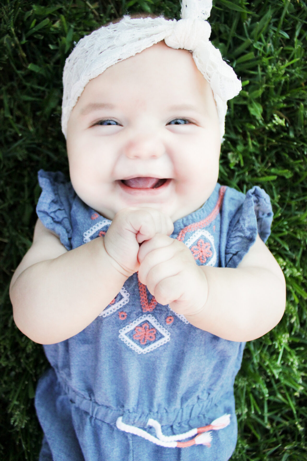 6 month old girl looking into camera while lying in the grass laughing