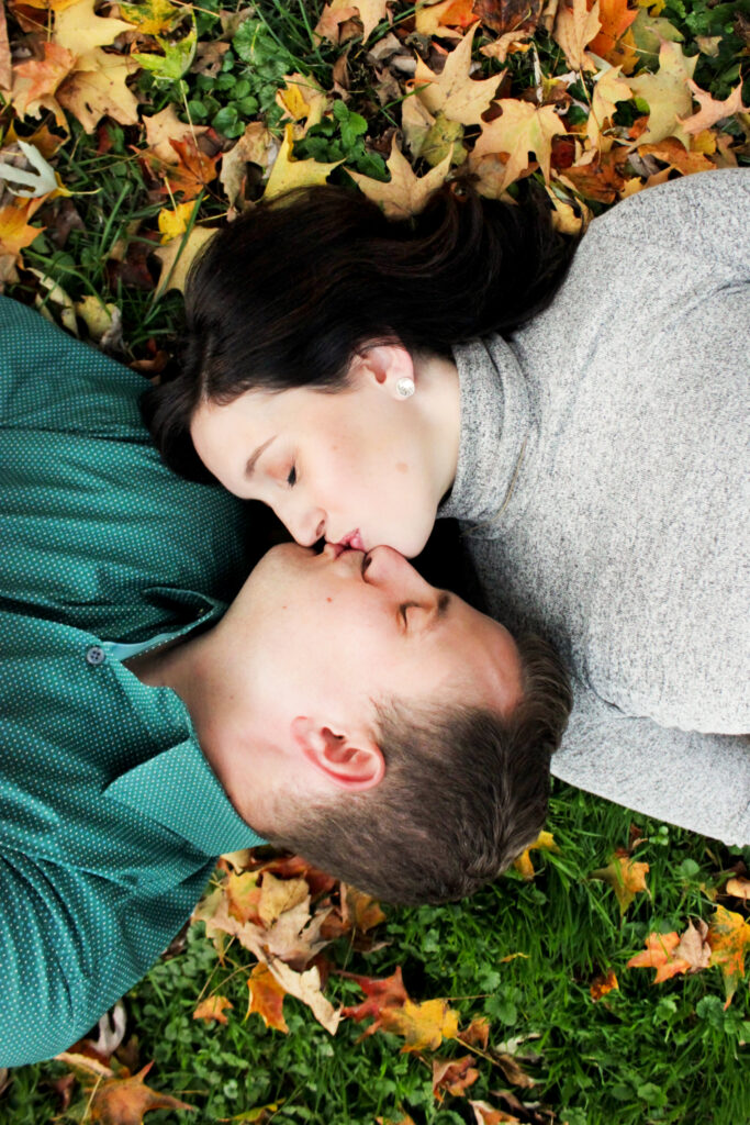 Married couple lying in autumn leaves kissing