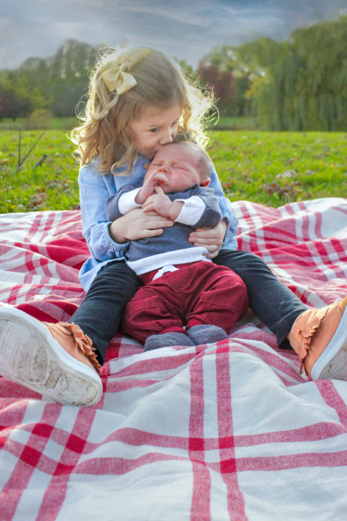 Little girl holding baby brother on plaid blanket, kissing his head