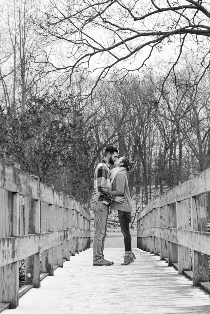 Young couple on wooden bridge in winter kissing for engagement photo