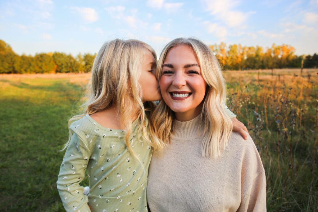 Young smiling mother getting kissed on the cheek by young daughter during autumn