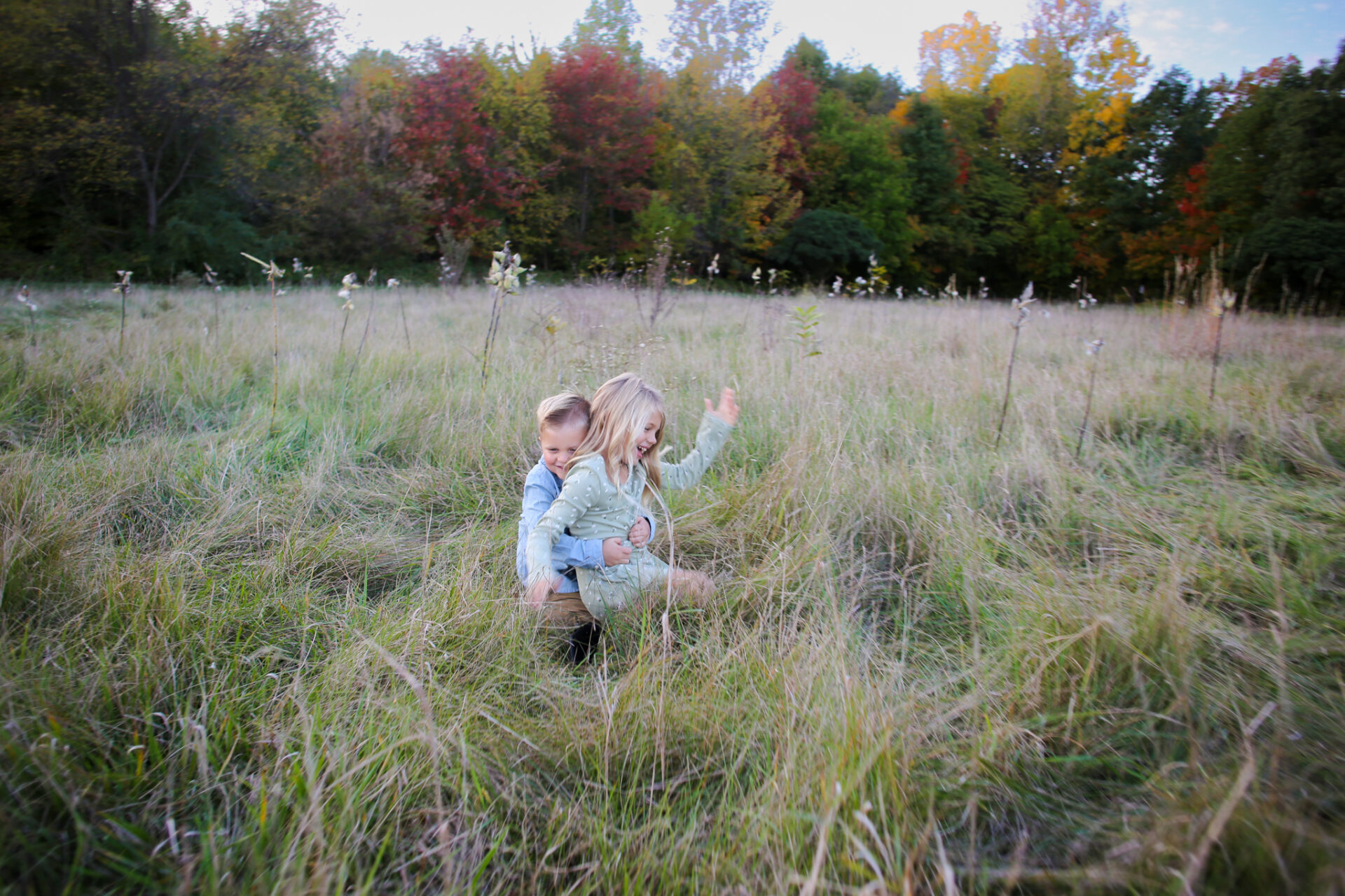 Young brother wrestles and hugs young sister in grass during autumn