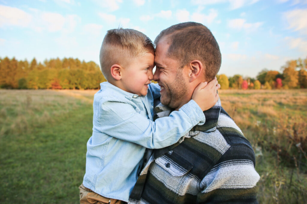 Young father holds young son, foreheads and noses pressed together and scrunching faces