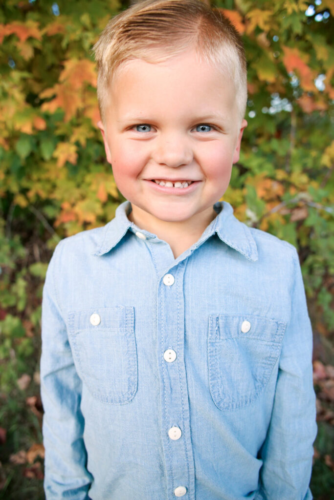 Young boy smiles at camera in front of fall leaves