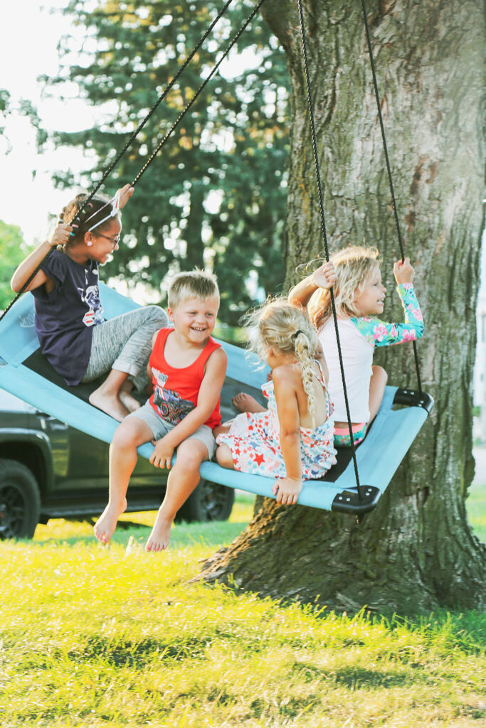 Group of young kids laughing on swing hanging from tree