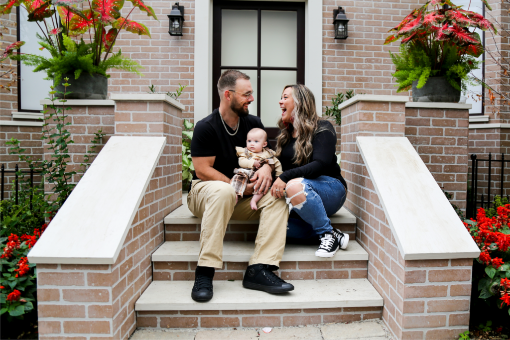 young couple sit on stairs and hold small baby, laughing