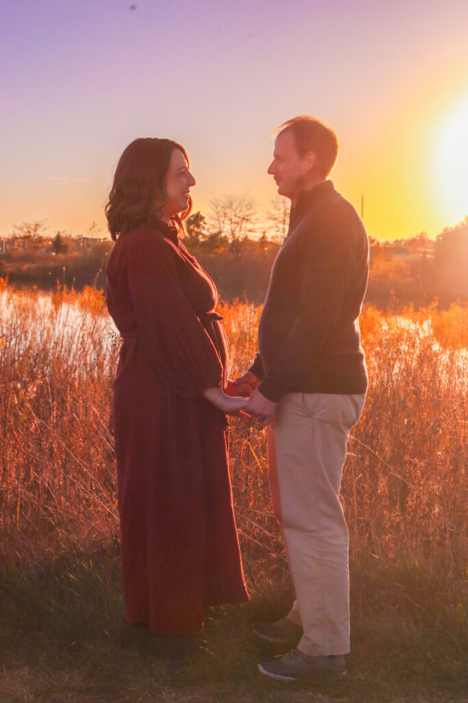 pregnant couple holds hands in golden hour