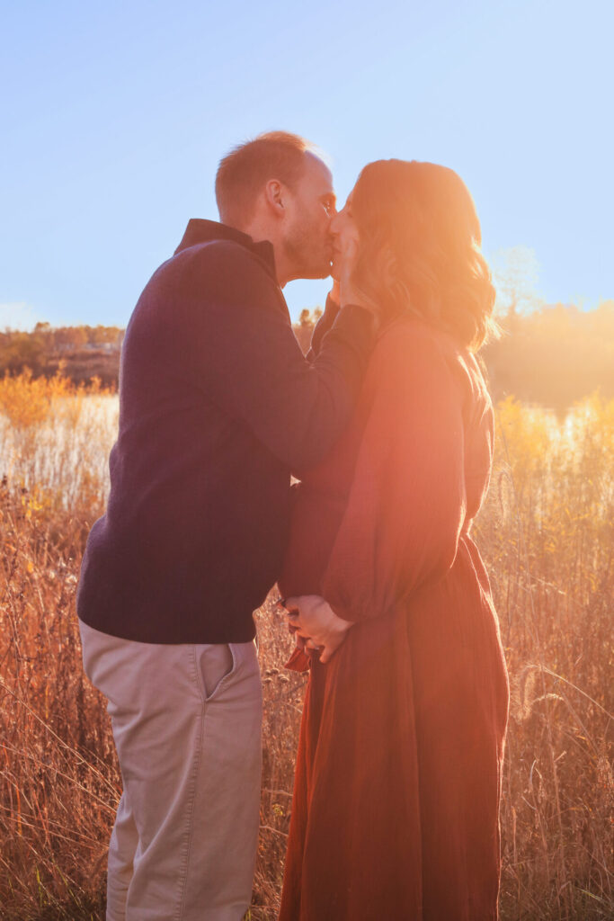 pregnant couple kiss in sunset, wife holds belly