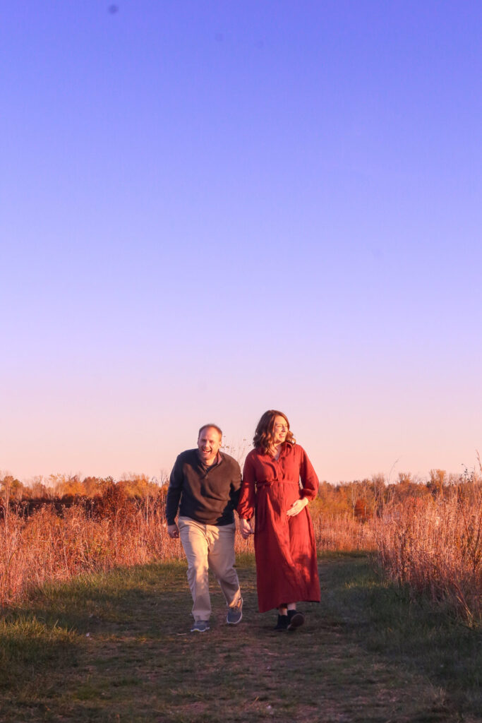 pregnant couple walk holding hands laughing